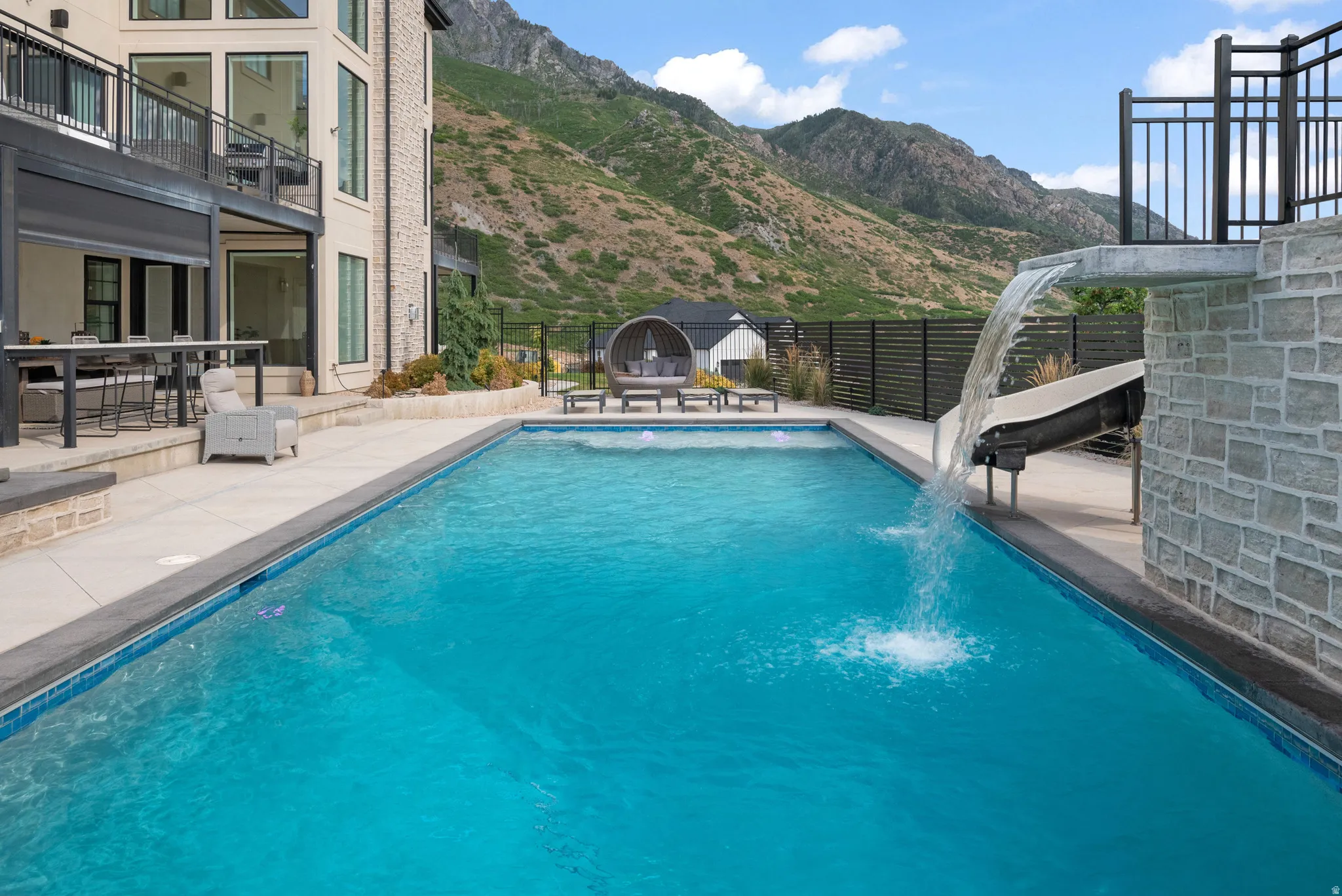 Expansive backyard featuring a rectangular swimming pool with a waterfall and slide, complemented by a large patio area with outdoor seating