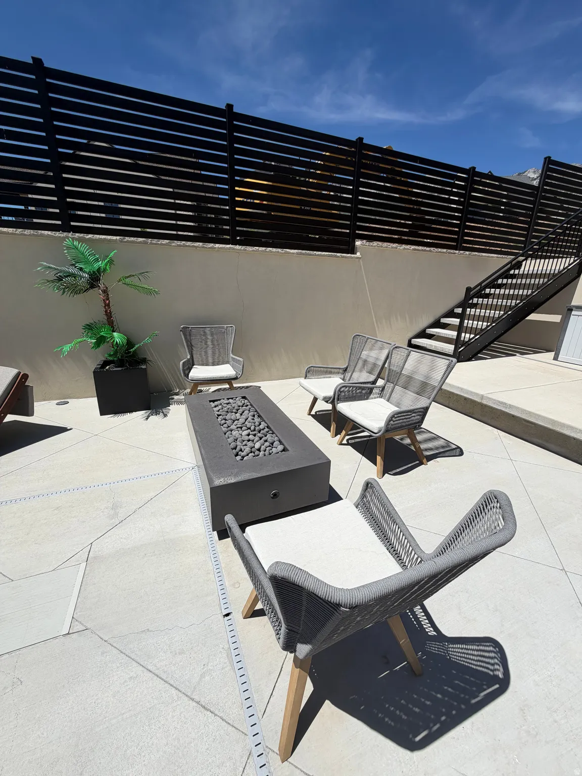 Outdoor patio featuring a rectangular fire pit with decorative stones, surrounded by light-toned pavers