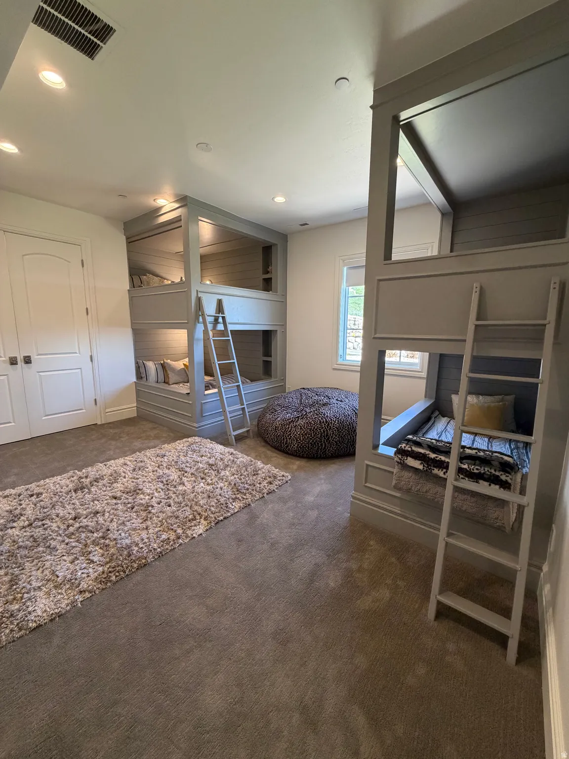 Room featuring built-in bunk beds with integrated shelving and ladders, recessed lighting, carpet flooring, and a window with natural light