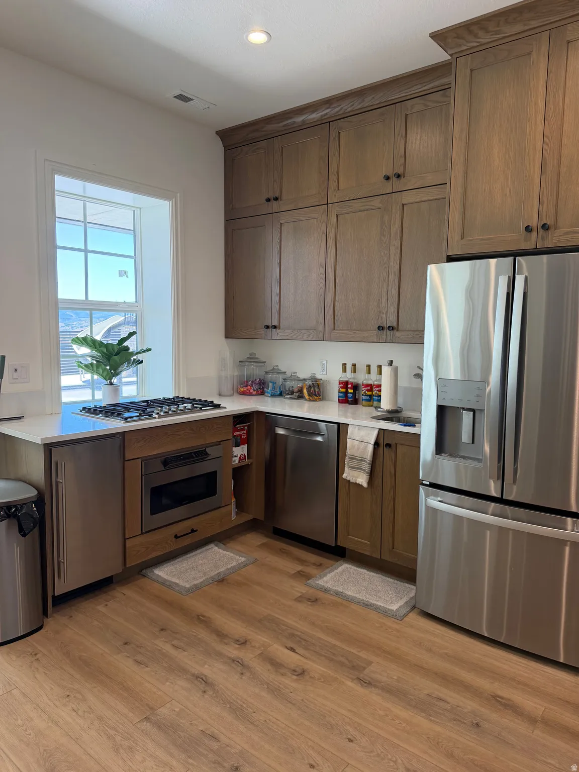 Modern kitchen featuring wood-finish flooring, white countertops, built-in stainless steel appliances, and wood cabinetry with crown molding