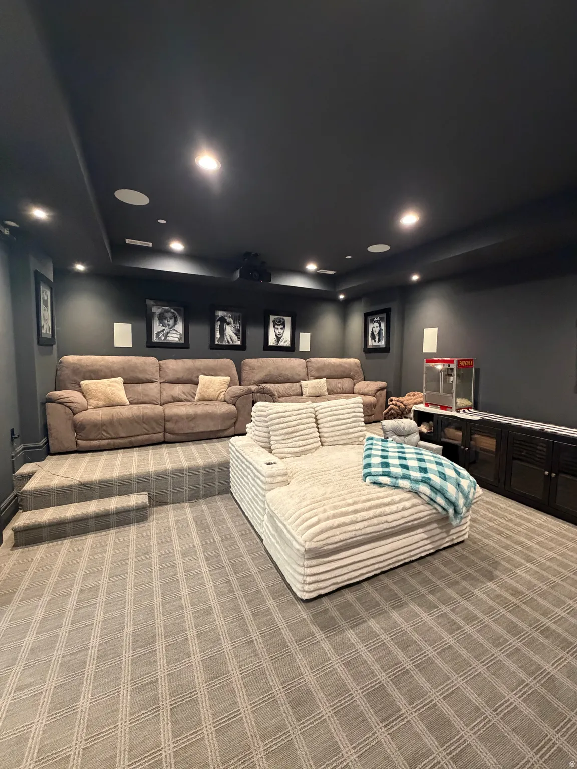 Dedicated media room featuring tiered seating, recessed lighting, ceiling-mounted projector, built-in speakers, and patterned carpet flooring