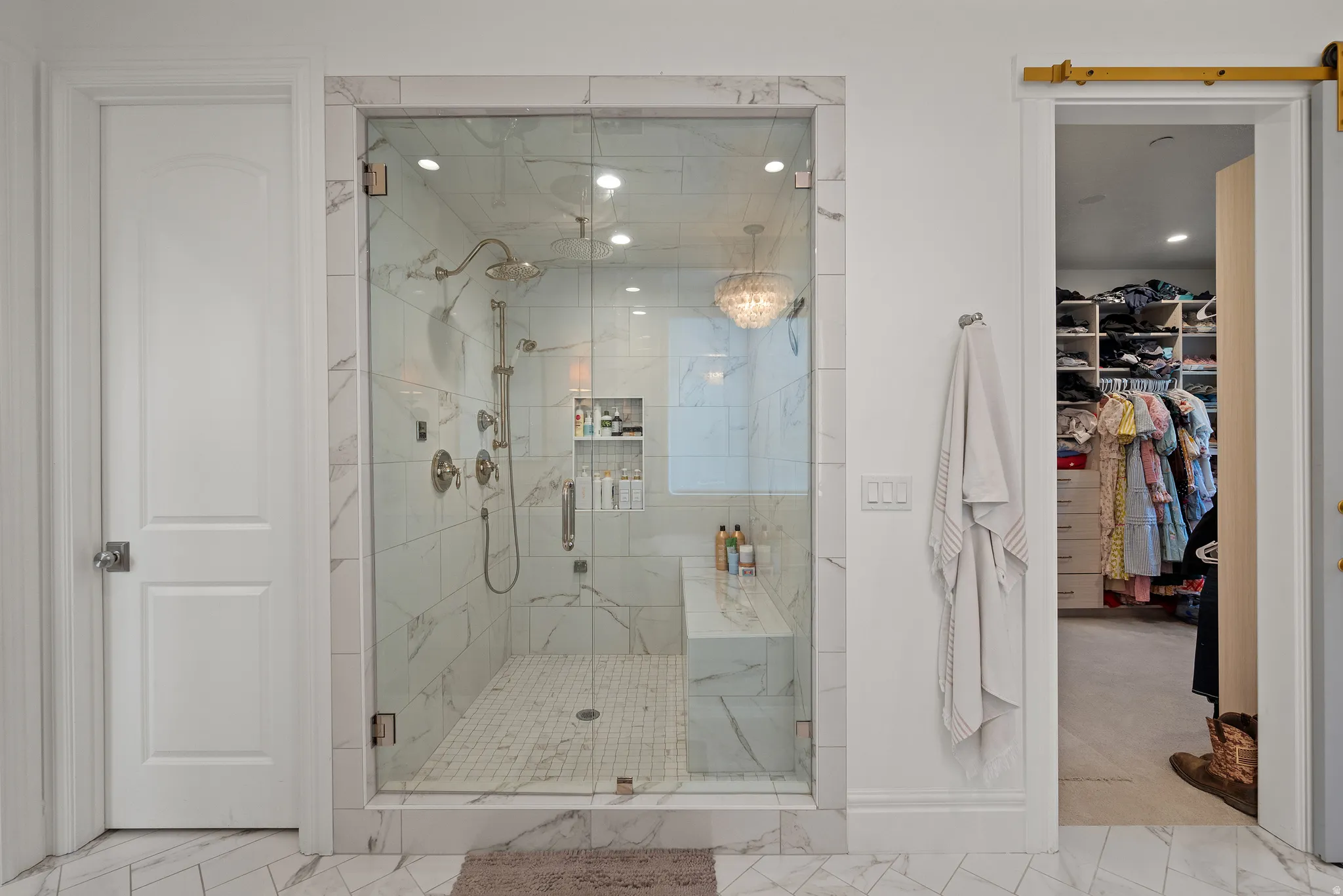 Glass-enclosed shower with a built-in bench and marble-style tile surround