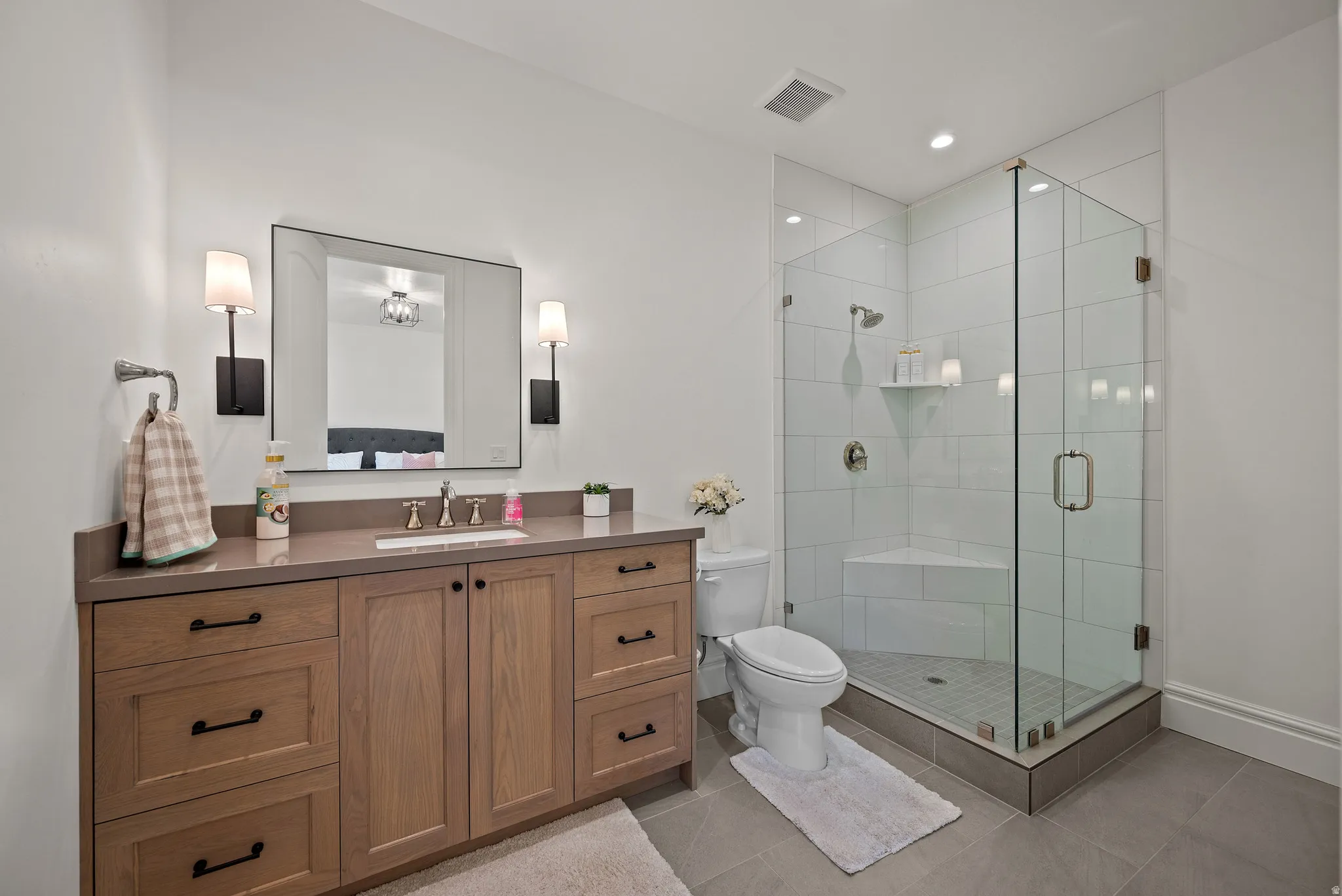 Contemporary bathroom featuring a glass-enclosed shower with a built-in bench, a single vanity with wood-finish cabinetry, a stone-finish countertop, and a large rectangular mirror with wall sconces