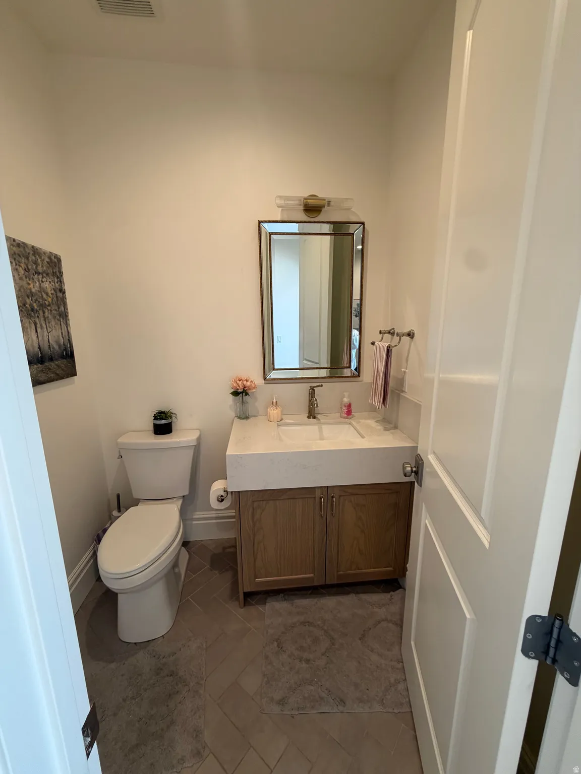 Bathroom featuring a wood-finish vanity with integrated sink, rectangular framed mirror, and contemporary wall-mounted light fixture
