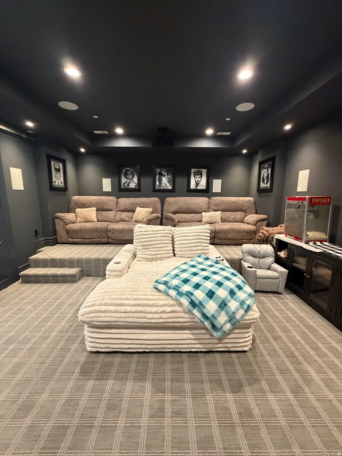 Dedicated entertainment room featuring layered seating, recessed ceiling lighting, wall-mounted speakers, a ceiling-mounted projector, and patterned carpet flooring