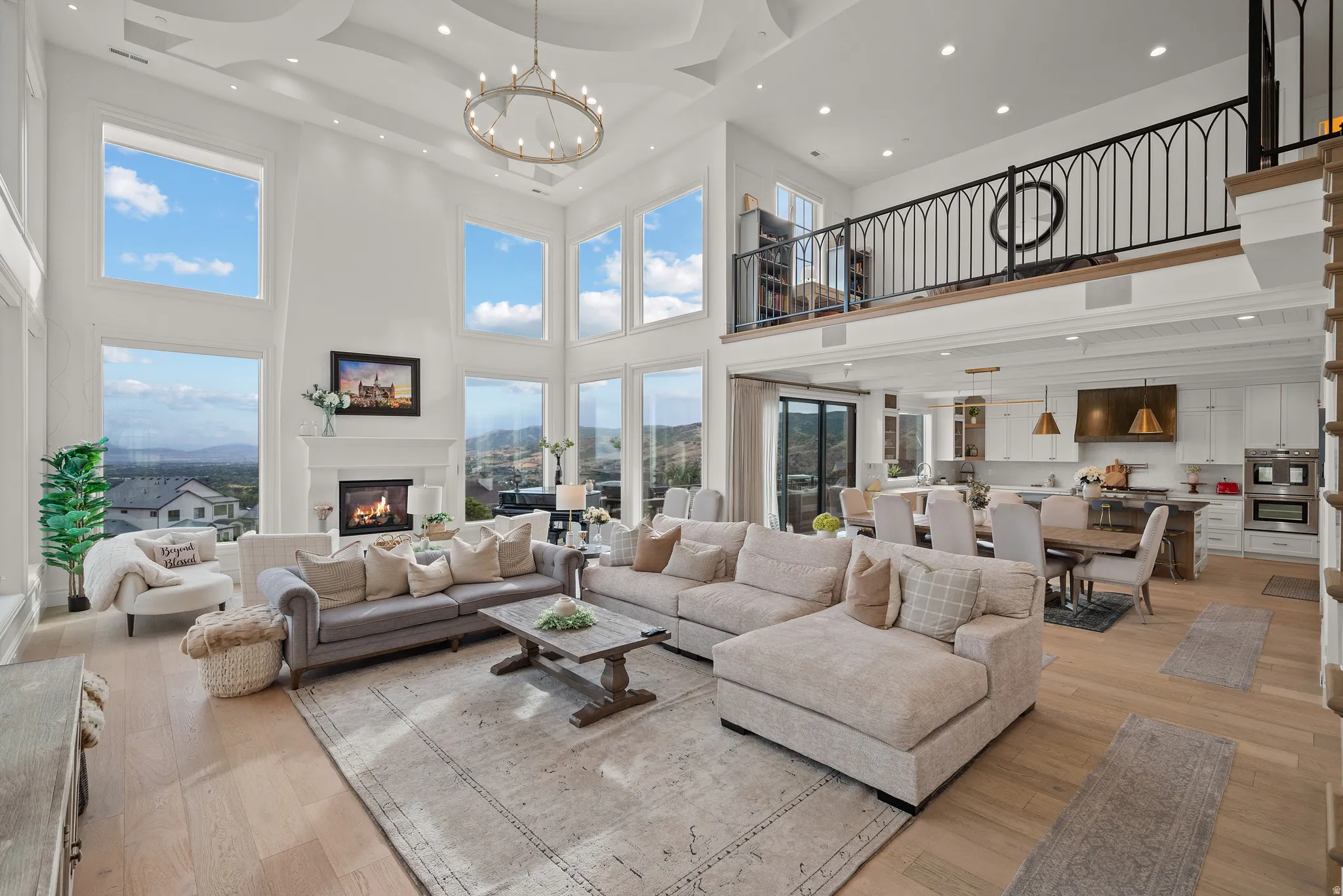 Grand living space featuring a two-story ceiling, a tiered chandelier, abundant natural light from expansive windows, and a built-in fireplace