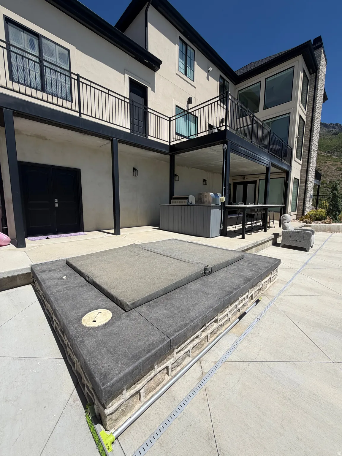 Expansive outdoor patio featuring a built-in hot tub, an outdoor kitchen with a grill, and substantial upper-level balconies with black railings