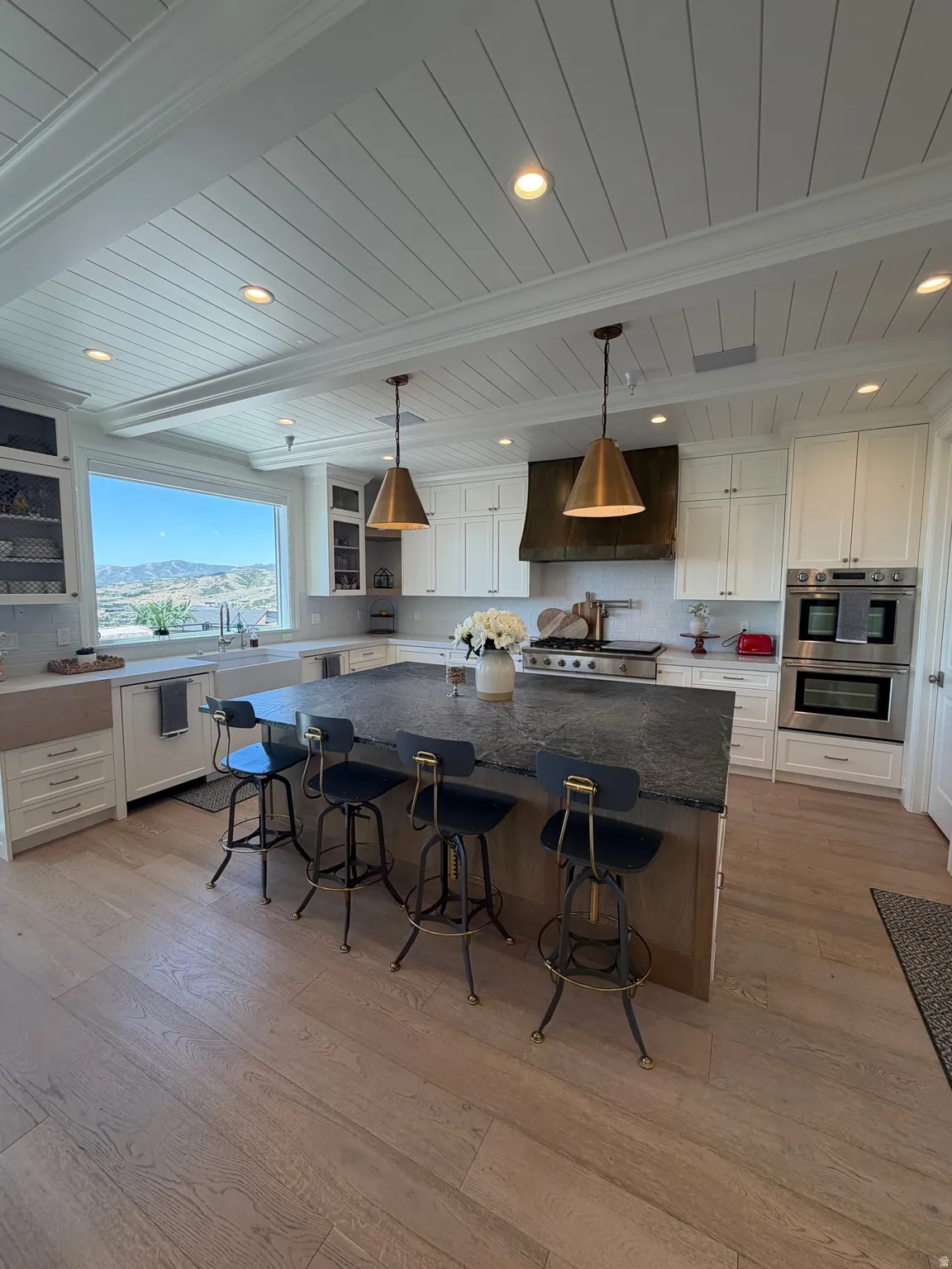 Spacious kitchen featuring white shaker cabinetry, an expansive center island with dark countertops, built-in stainless steel double ovens, and wood-finish flooring