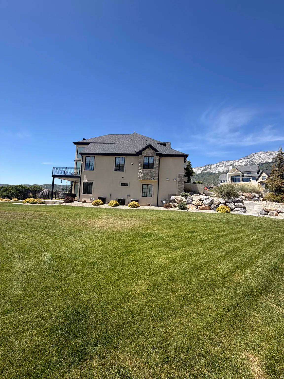 Expansive green lawn with a contemporary multi-story residence featuring a stucco and stone exterior