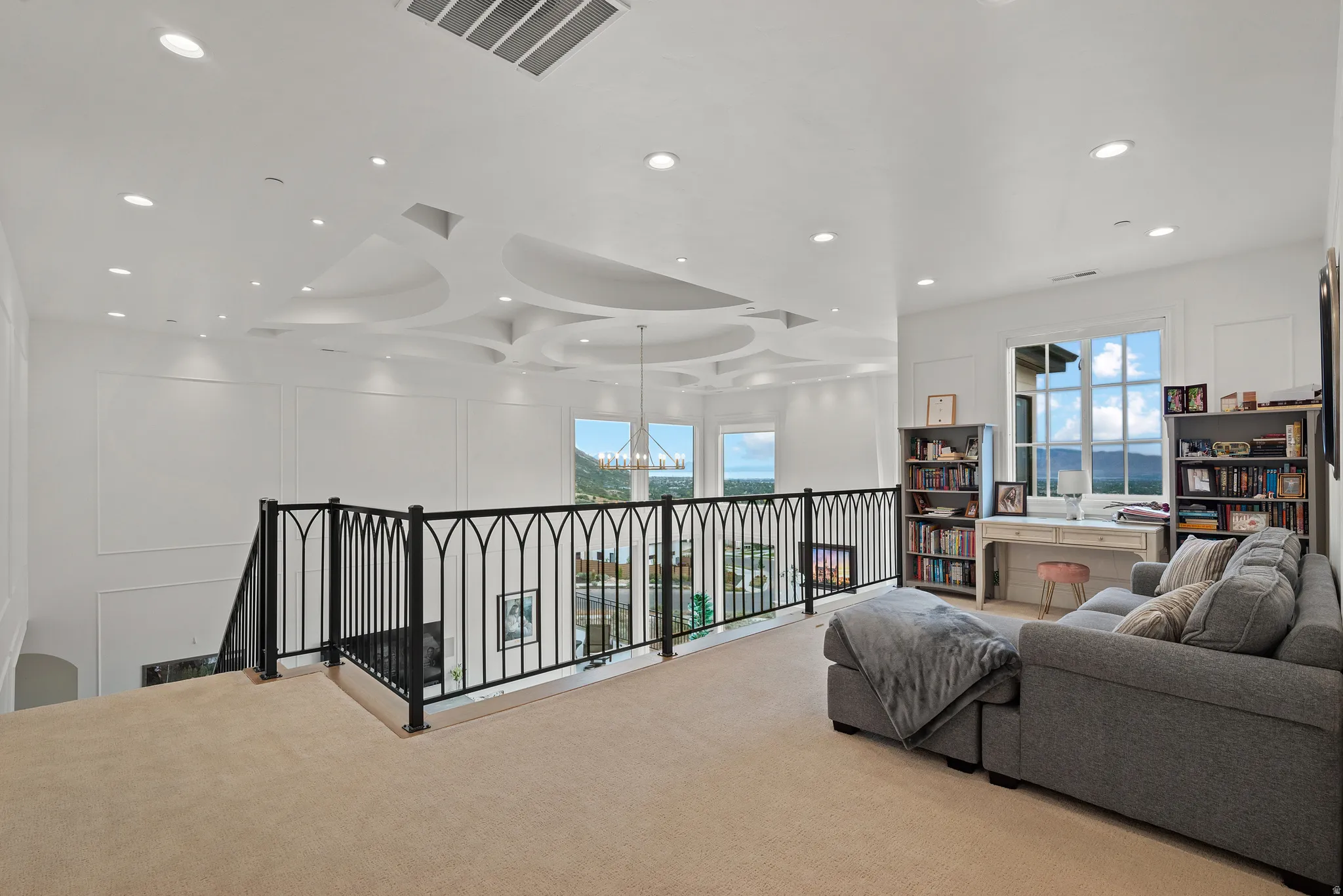 Loft space featuring a decorative ceiling design with recessed lighting, an ornate black metal railing, and large windows