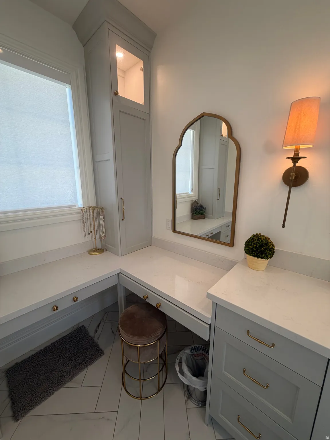 Built-in vanity with quartz countertops, custom gray cabinetry, and brass hardware