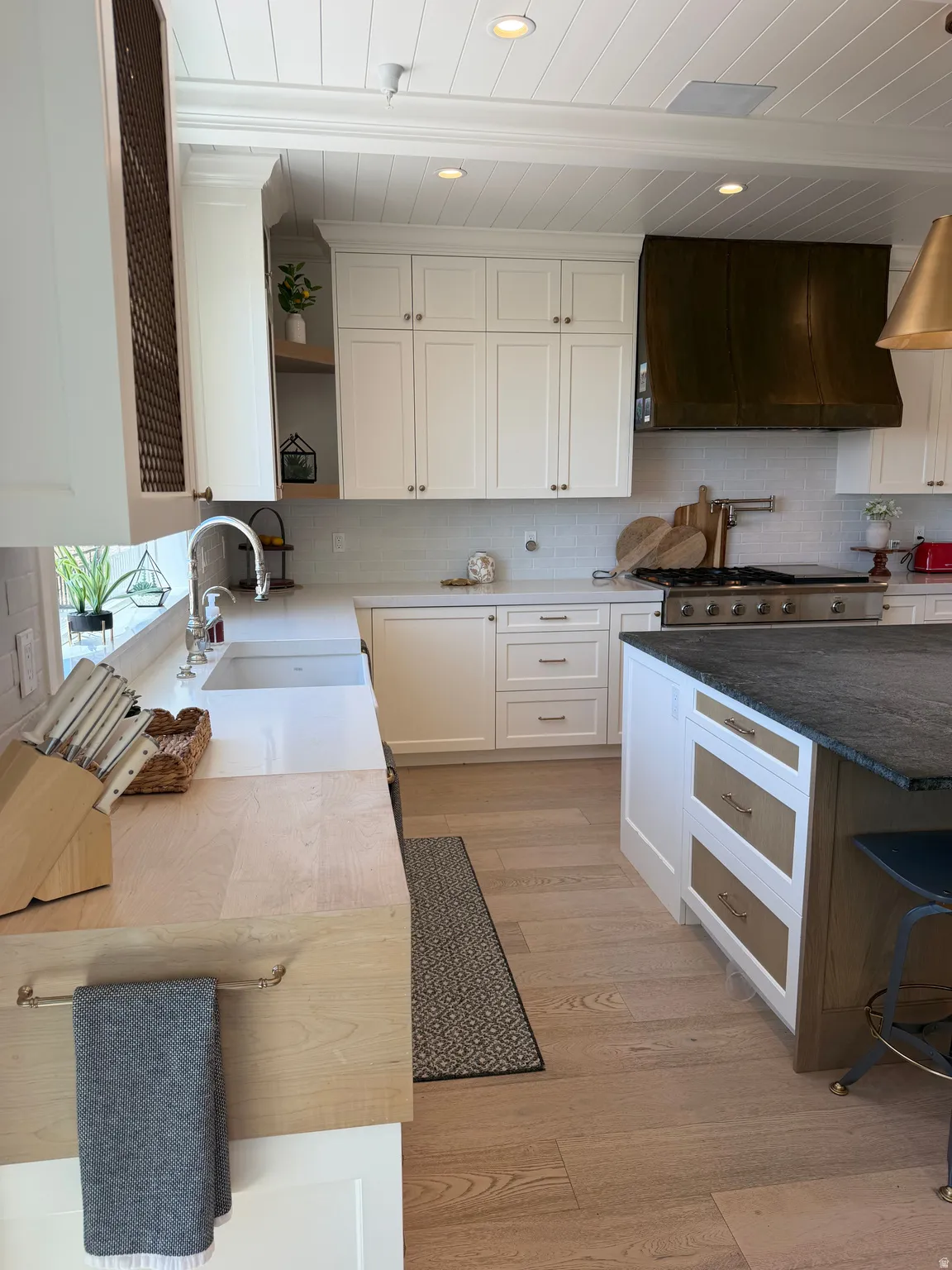 Gourmet kitchen featuring a substantial island with dark countertop, light wood-finish flooring, white shaker cabinetry, a stainless steel range, and a copper-toned range hood
