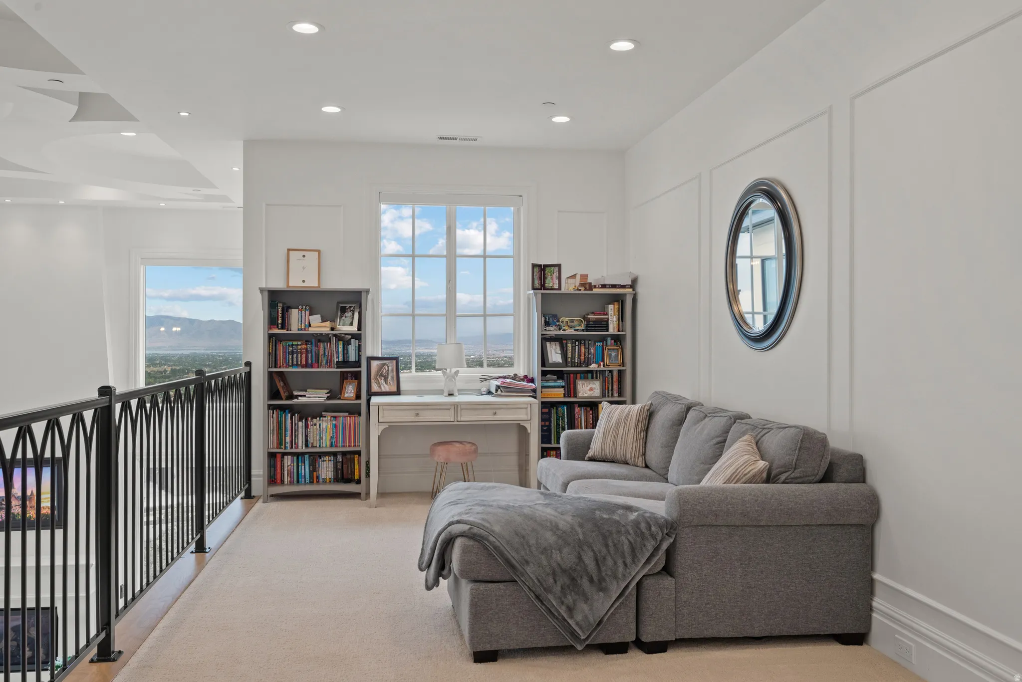 Loft space featuring a decorative black metal railing, window with distant mountainous scenery, recessed lighting, and wall panel molding