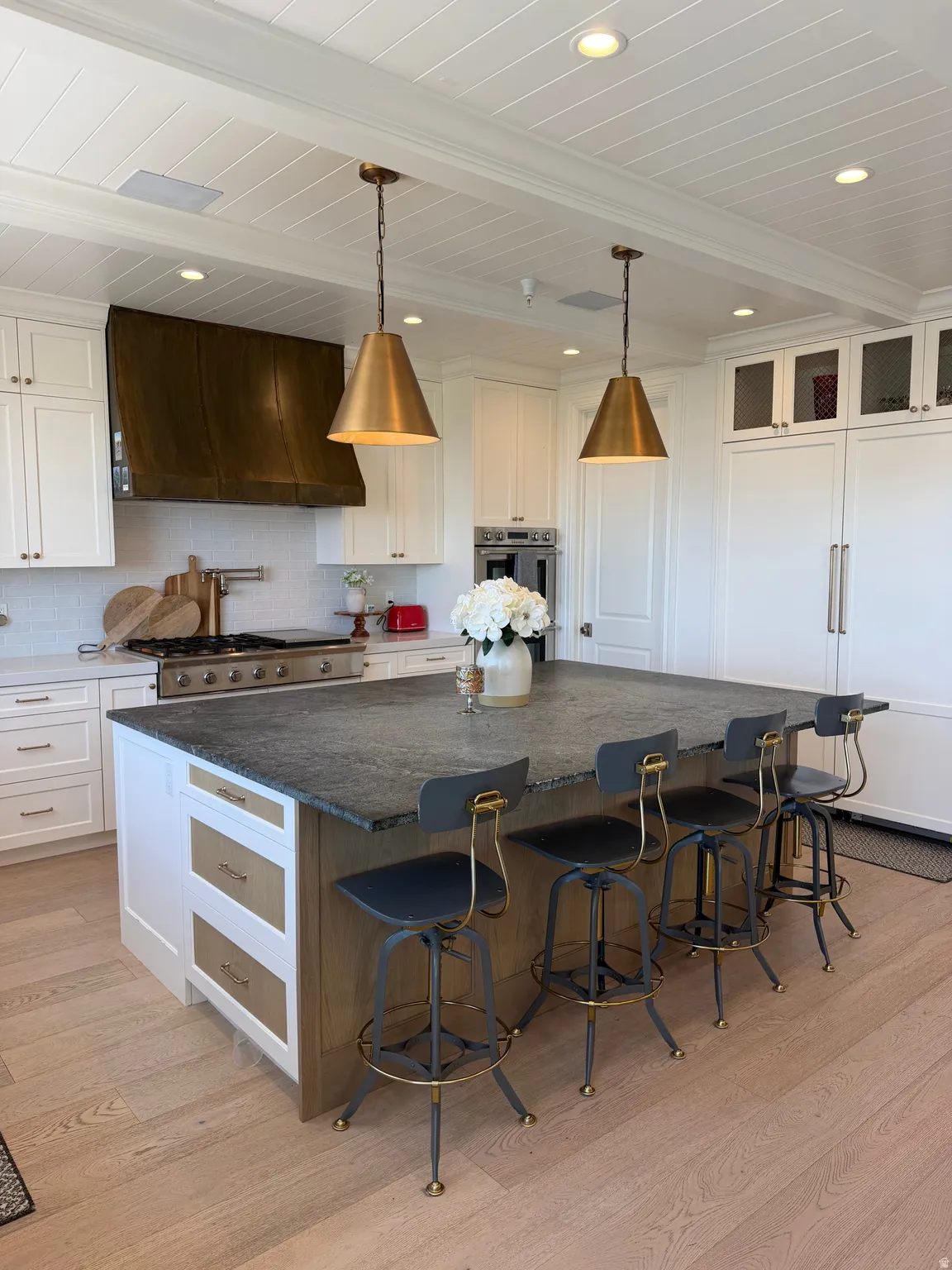Kitchen featuring a large central island with seating, pendant lighting, stainless steel appliances, a custom range hood, and wood-finish flooring