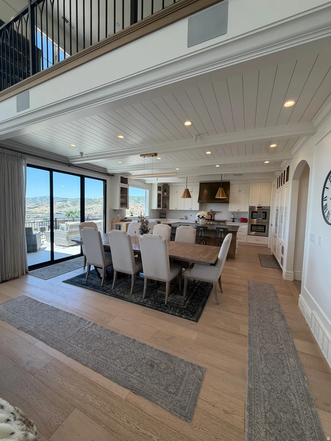 Open-concept living space with light wood-finish flooring, a shiplap ceiling, recessed lighting, and a second-story balcony with iron railings