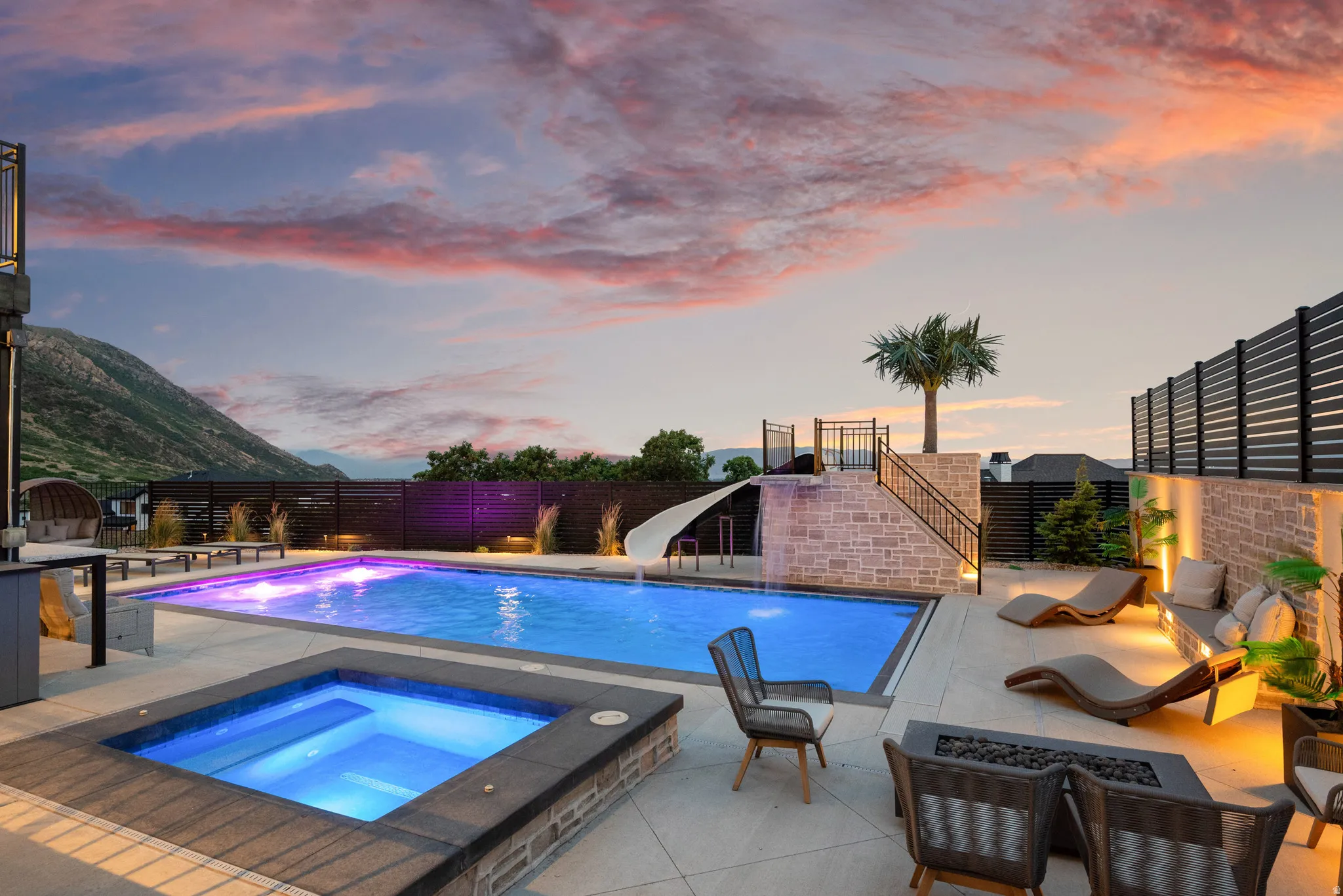 Resort-style backyard featuring a rectangular swimming pool with integrated lighting, a separate square spa, and a stone-clad water slide structure