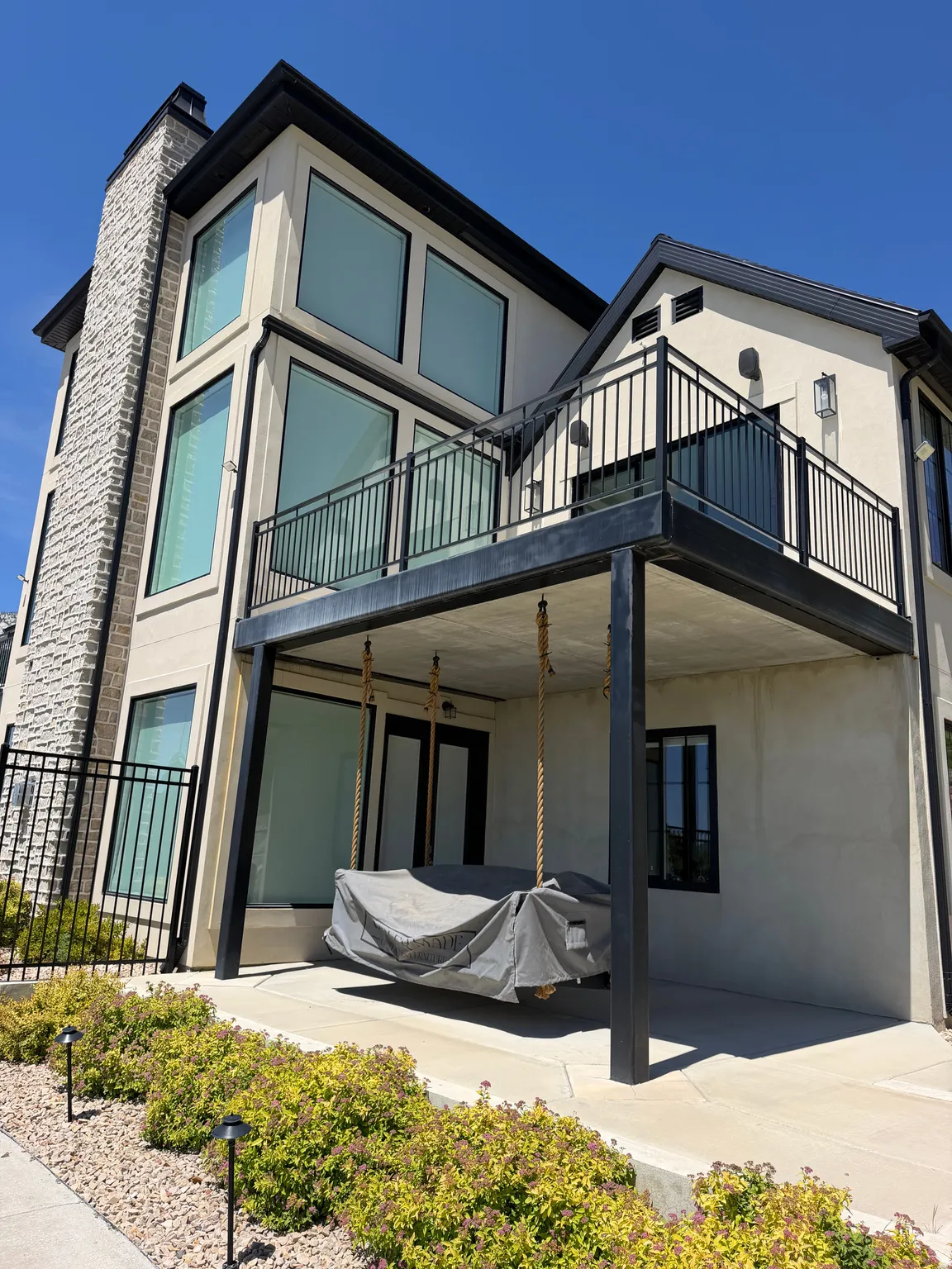 Modern stucco exterior featuring a stone-clad chimney and a balcony with black metal railings