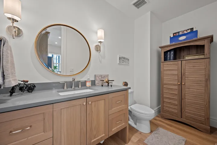 Bathroom featuring a light wood-finish vanity with a built-in sink and gray countertop, complemented by a round framed mirror