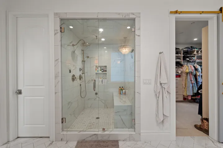 Glass-enclosed shower with a built-in bench and marble-style tile surround