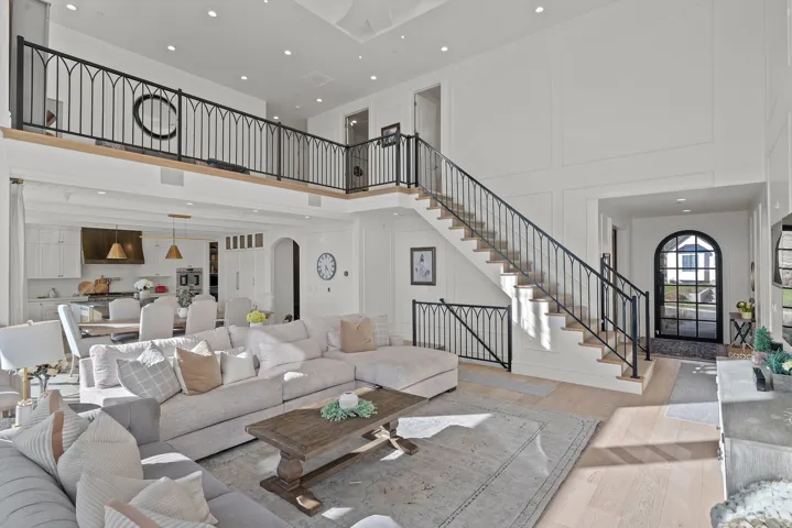 Two-story living area featuring a grand staircase with custom wrought iron railings, an open concept kitchen with a large island, wood-finish flooring, and high ceilings with recessed lighting