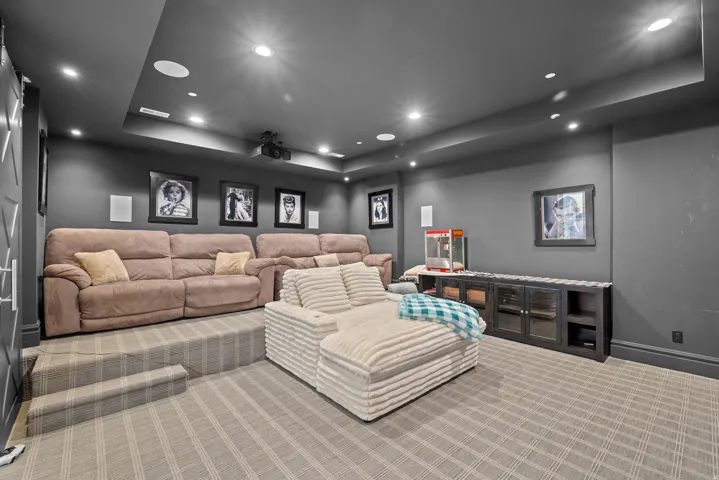 Dedicated media room featuring tiered seating, recessed lighting, a ceiling-mounted projector, and integrated ceiling speakers