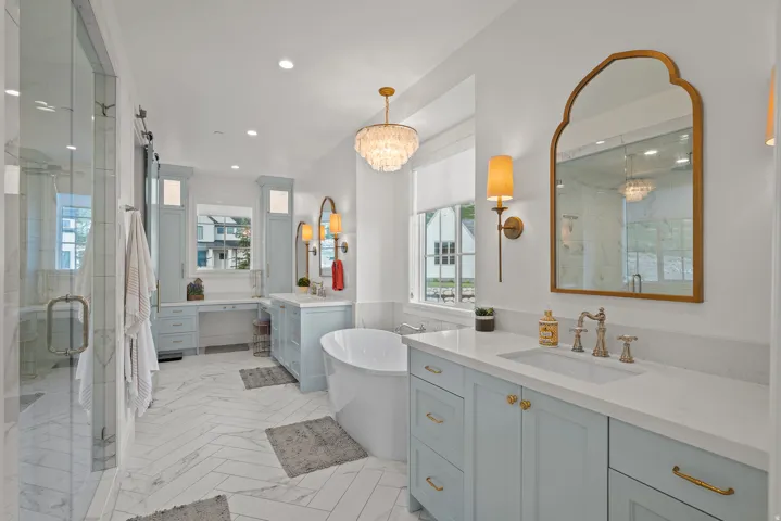 Spacious bathroom featuring a freestanding soaking tub, dual vanity with light blue cabinetry, a glass-enclosed shower, and herringbone pattern tile flooring