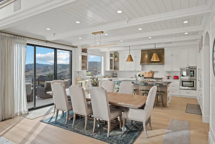 Open-concept kitchen and dining area featuring light wood-finish flooring, white shiplap ceilings with recessed lighting, and expansive glass sliding doors