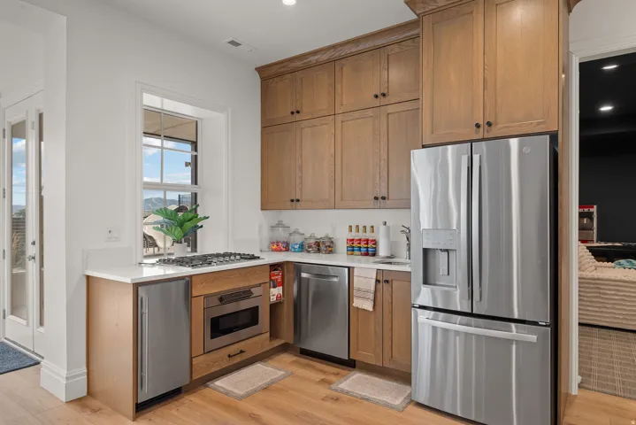 Kitchenette featuring wood-finish flooring, light wood cabinetry, white countertops, and stainless steel appliances including a refrigerator, dishwasher, and microwave