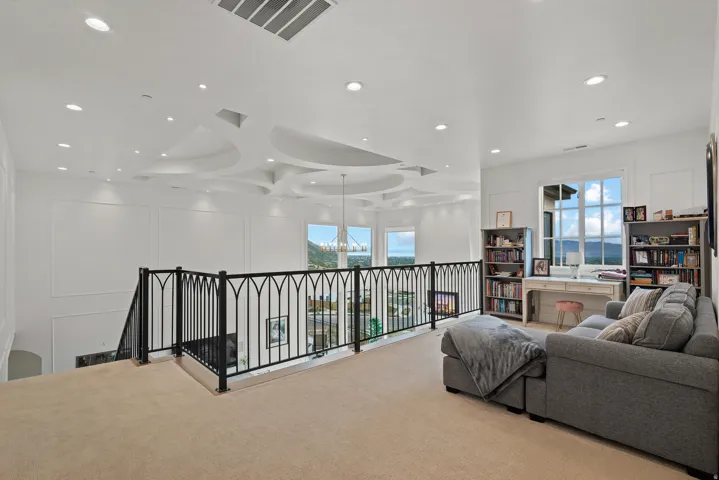 Loft space featuring a decorative ceiling design with recessed lighting, an ornate black metal railing, and large windows