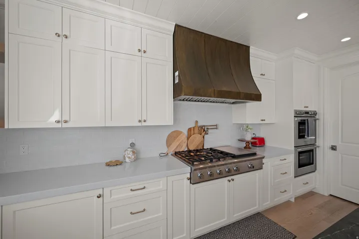 Kitchen featuring white shaker cabinetry, stainless steel gas range with griddle, custom dark metal range hood, light-toned countertops, and subway tile backsplash