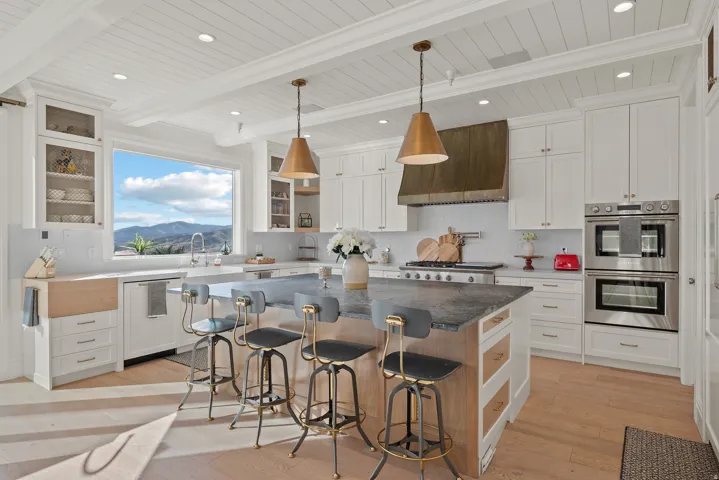 Spacious kitchen featuring an expansive window, shiplap ceiling, white cabinetry, integrated double ovens, and a large central island with a dark countertop