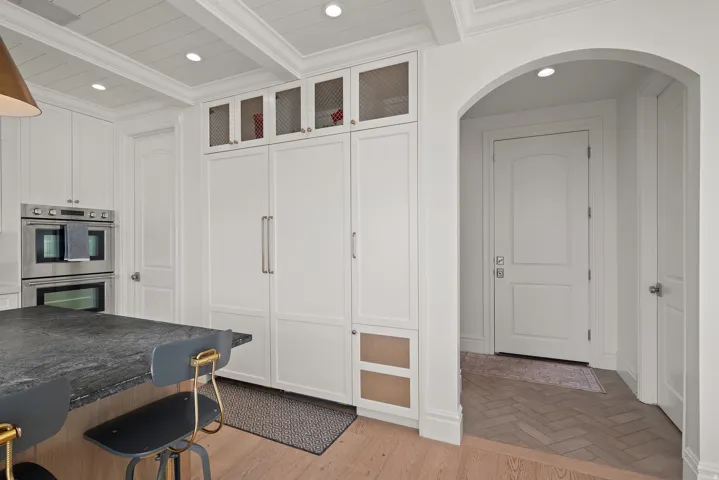Kitchen featuring integrated panel-front appliances, double wall ovens, a coffered ceiling with recessed lighting, and an arched entryway