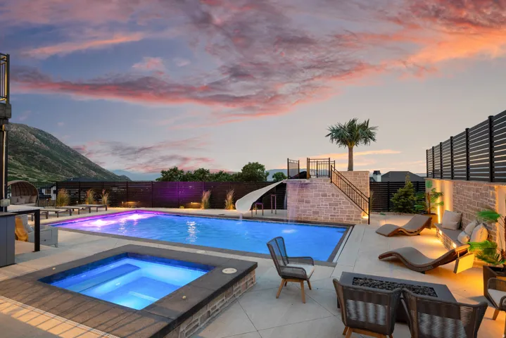 Resort-style backyard featuring a rectangular swimming pool with integrated lighting, a separate square spa, and a stone-clad water slide structure