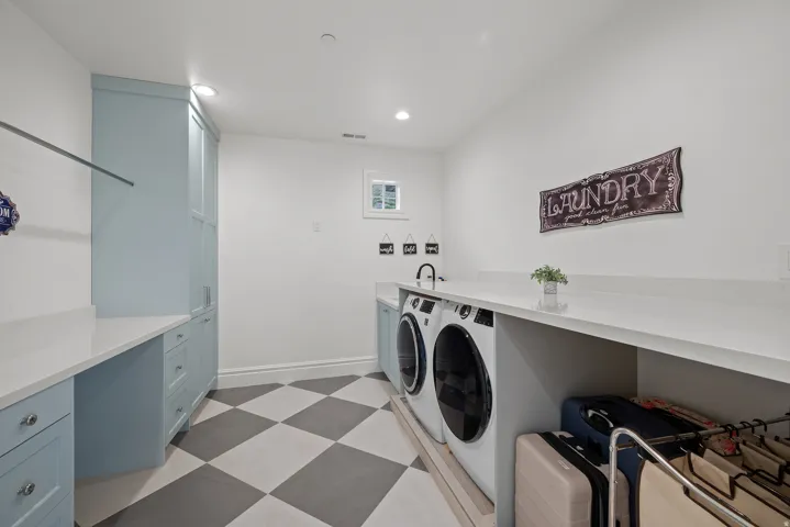 Laundry room featuring checkerboard flooring, light blue cabinetry, built-in countertops, a sink with a wall-mounted faucet, and a window