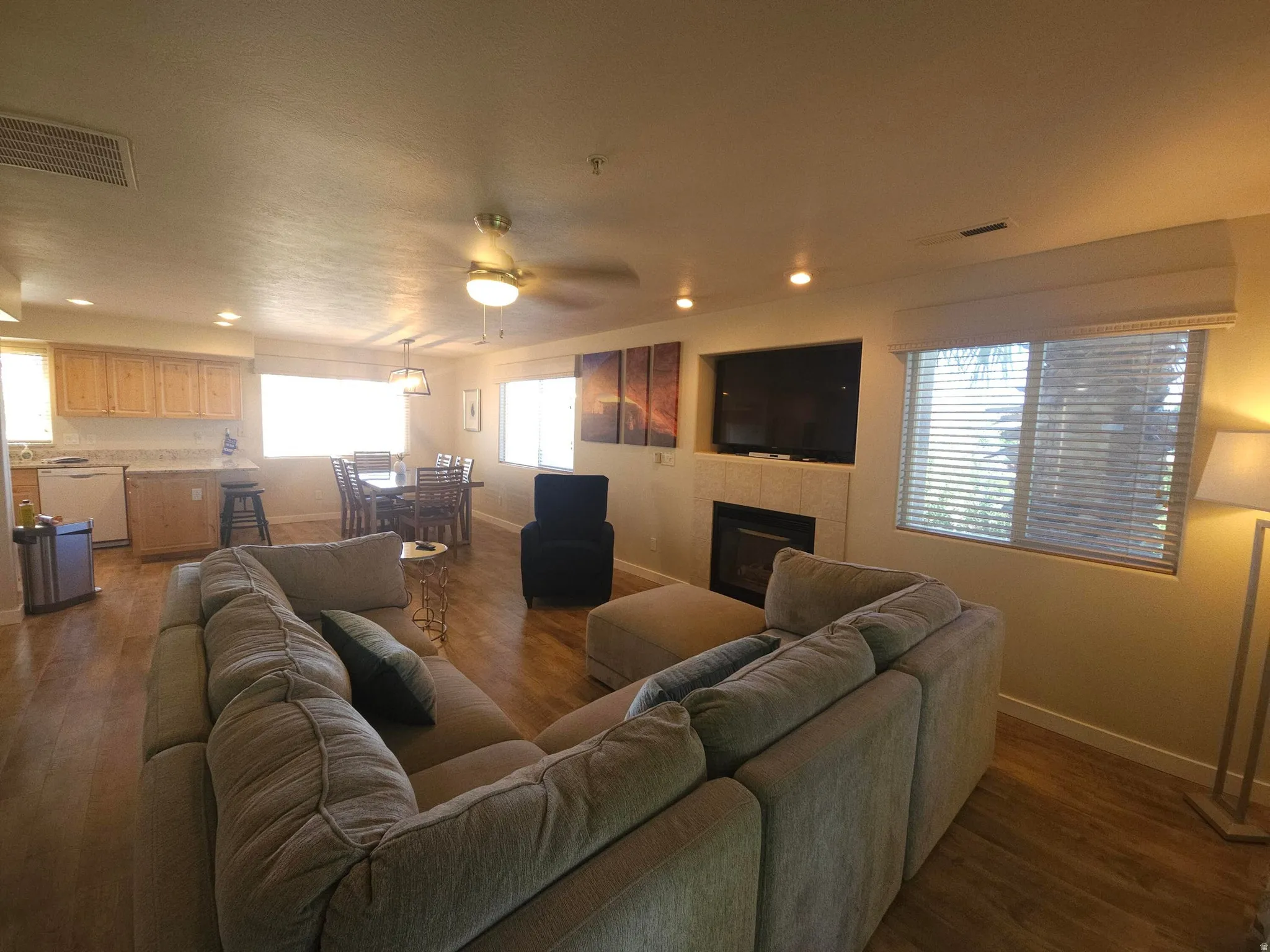 Integrated living space featuring wood-finish flooring, a built-in fireplace with a hearth, recessed lighting, a ceiling fan, and multiple windows with blinds