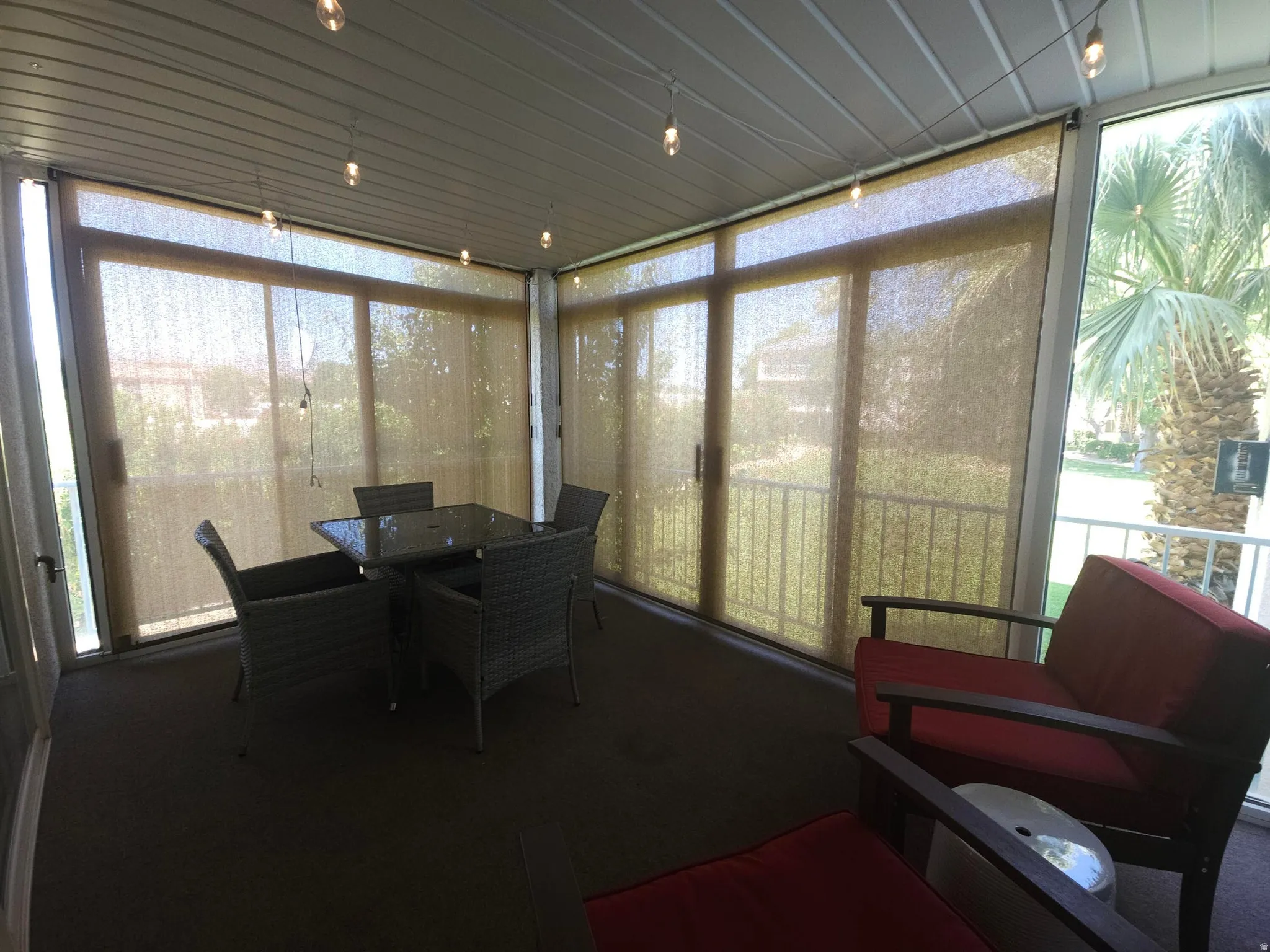 Enclosed patio featuring multiple sliding glass doors, neutral-toned roller shades, a slatted ceiling, and string lighting