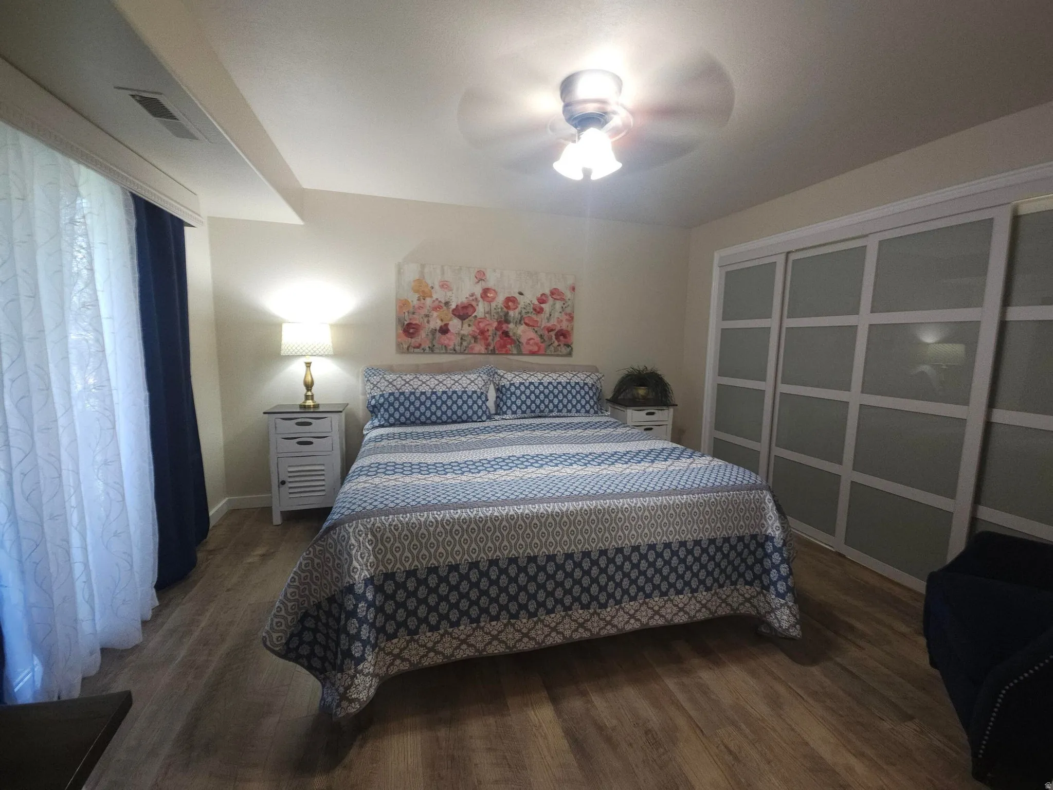 Bedroom featuring wood-finish flooring, a ceiling fan with integrated lighting, and a window with blinds