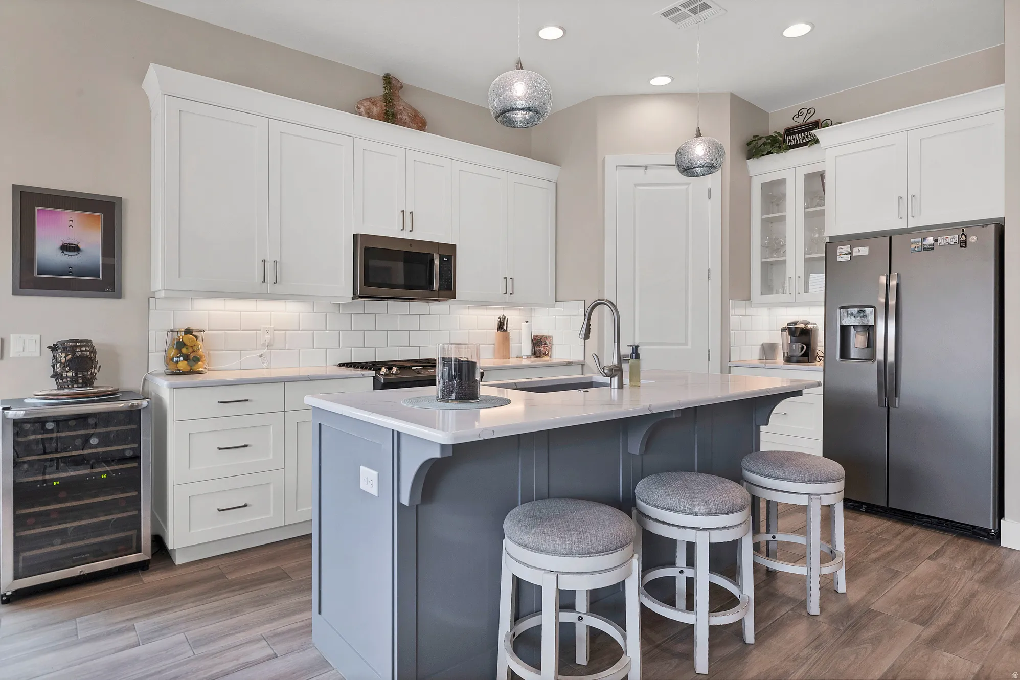 Modern kitchen featuring white shaker cabinetry, stainless steel appliances, a white subway tile backsplash, and a central island with a contrasting base and integrated sink