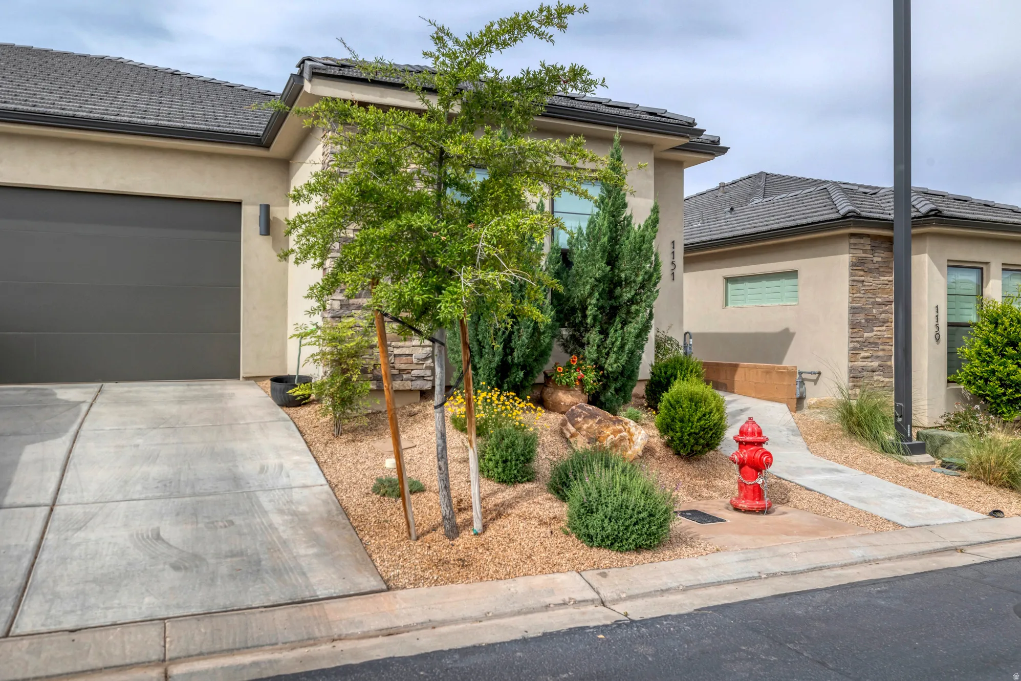 Contemporary stucco exterior featuring a stone accent wall, an attached garage, and a concrete driveway