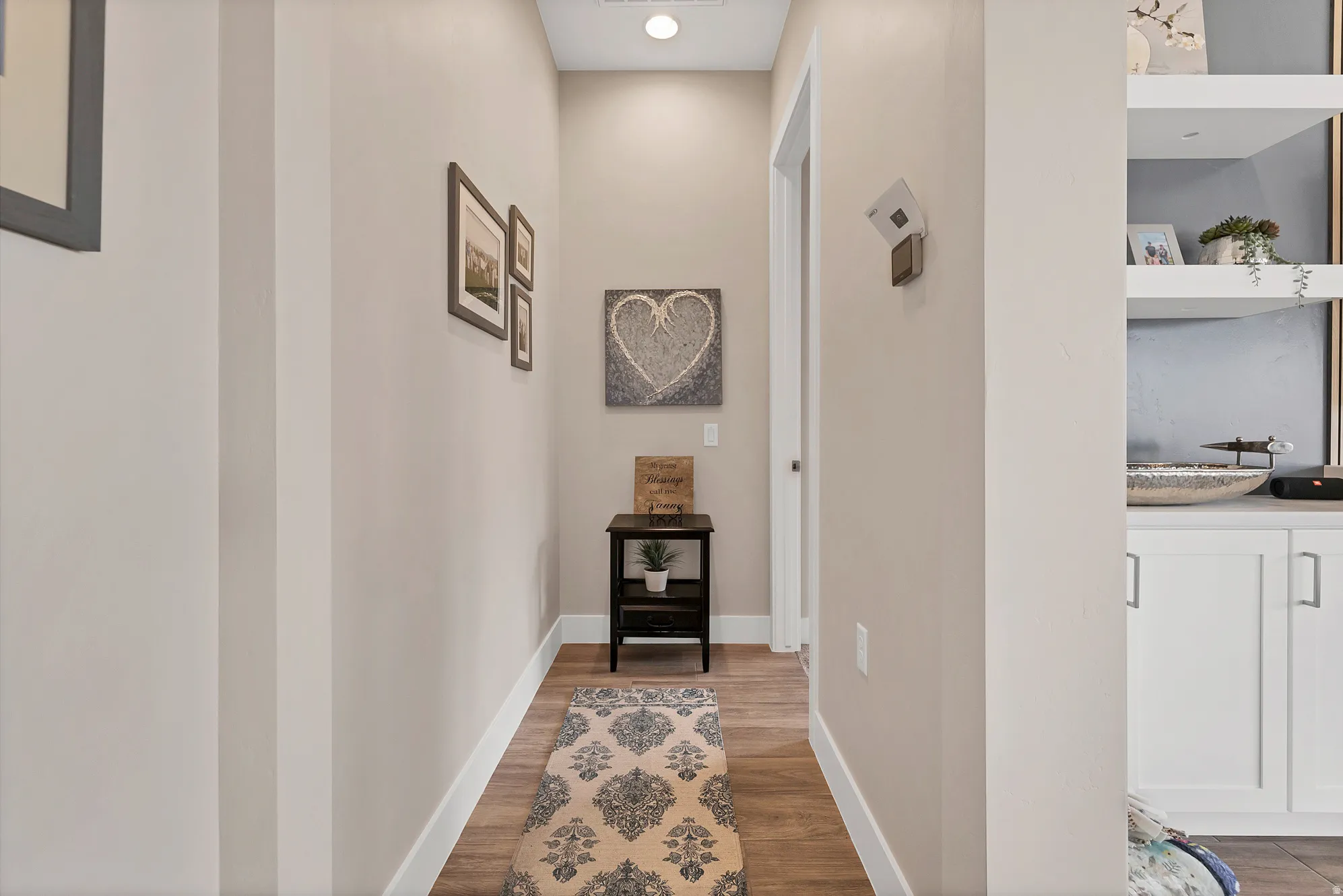 Hallway featuring light neutral wall paint, wood-finish flooring, and white baseboards