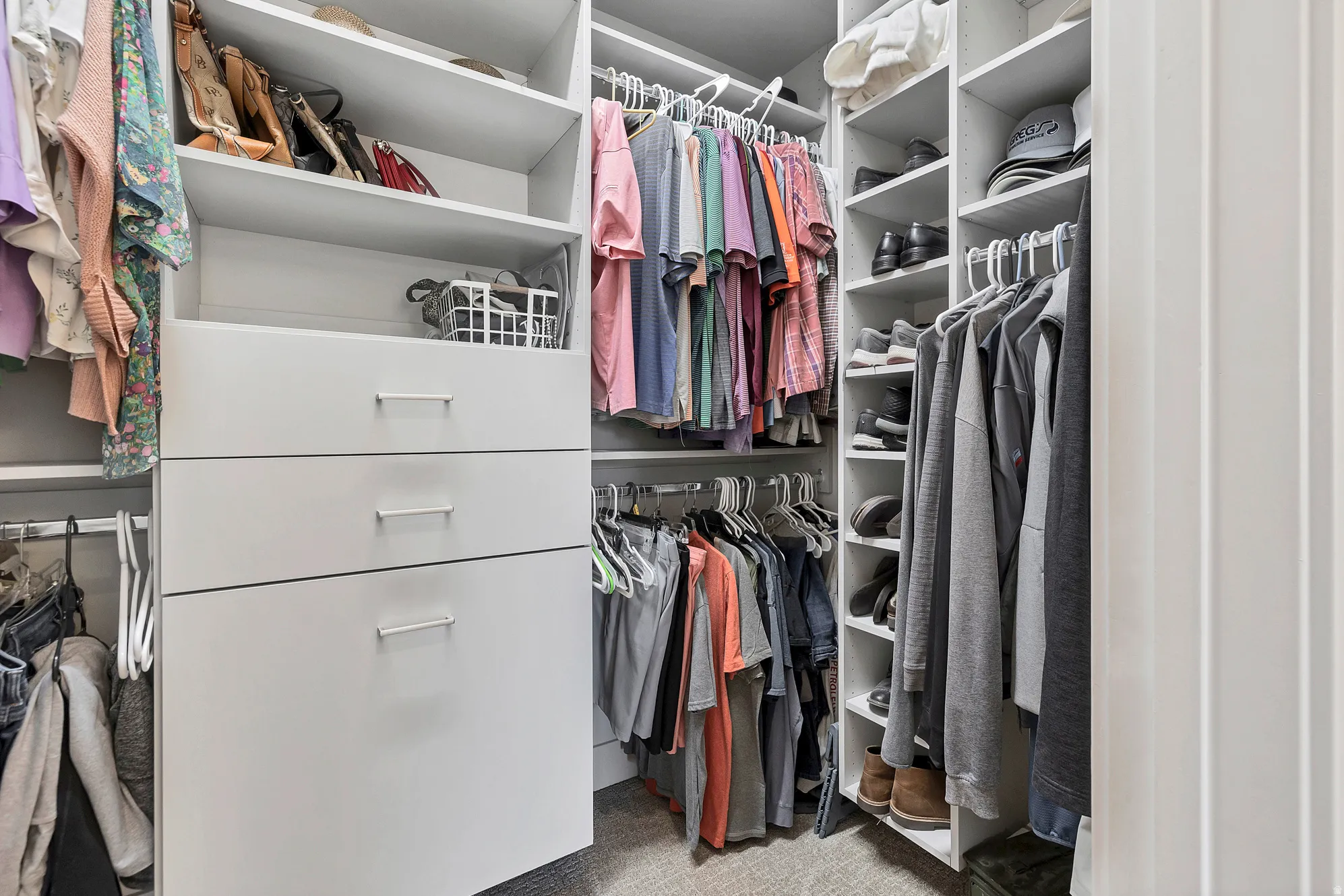 Custom closet system featuring white shelving, multiple hanging rods, integrated drawers with horizontal hardware, and dedicated shoe storage