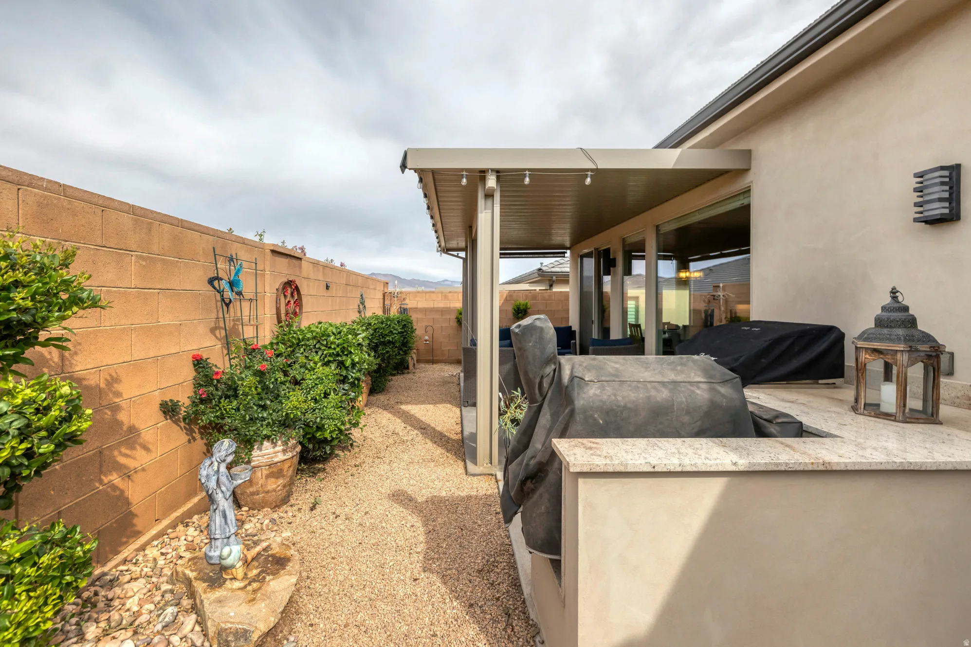 Outdoor kitchen with light-toned countertop, covered patio structure, and exterior wall lighting