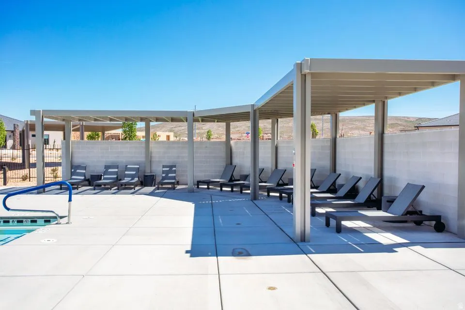 Swimming pool deck featuring a metal pergola, multiple chaise lounges, concrete block wall, and a blue pool handrail