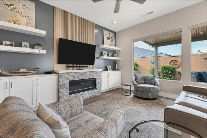 Living area featuring a textured accent wall, an electric fireplace with stone surround, custom built-in cabinetry, and large windows with outdoor views