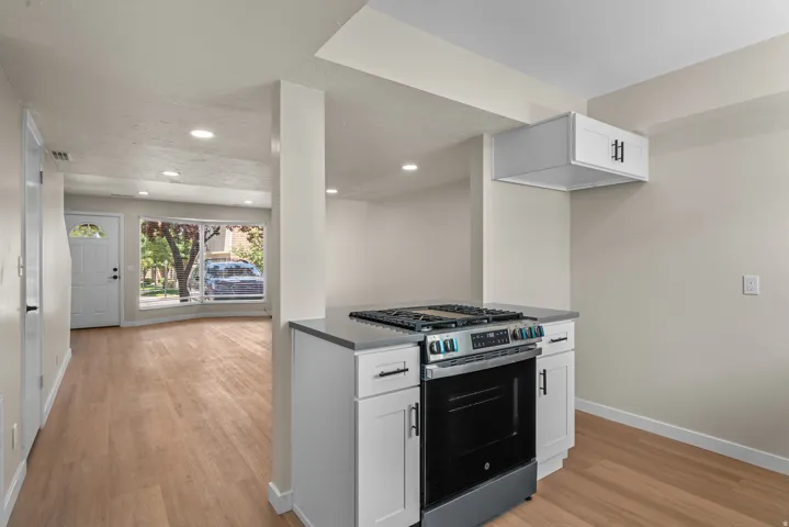 Kitchen island featuring a gas range, white cabinetry with dark hardware, and a stone-finish countertop