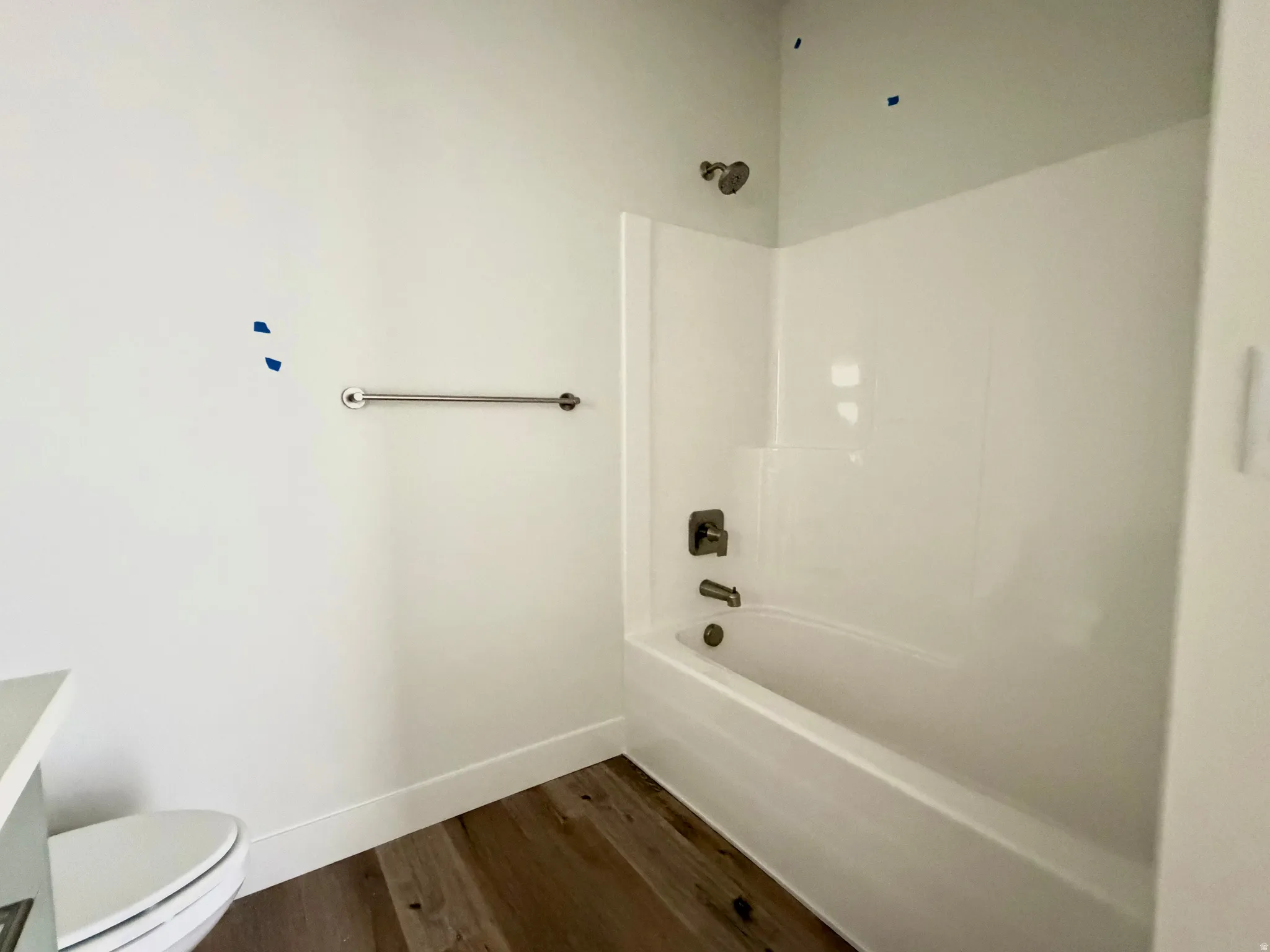 Bright bathroom featuring a white tub-shower combination, brushed nickel fixtures, and wood-finish flooring