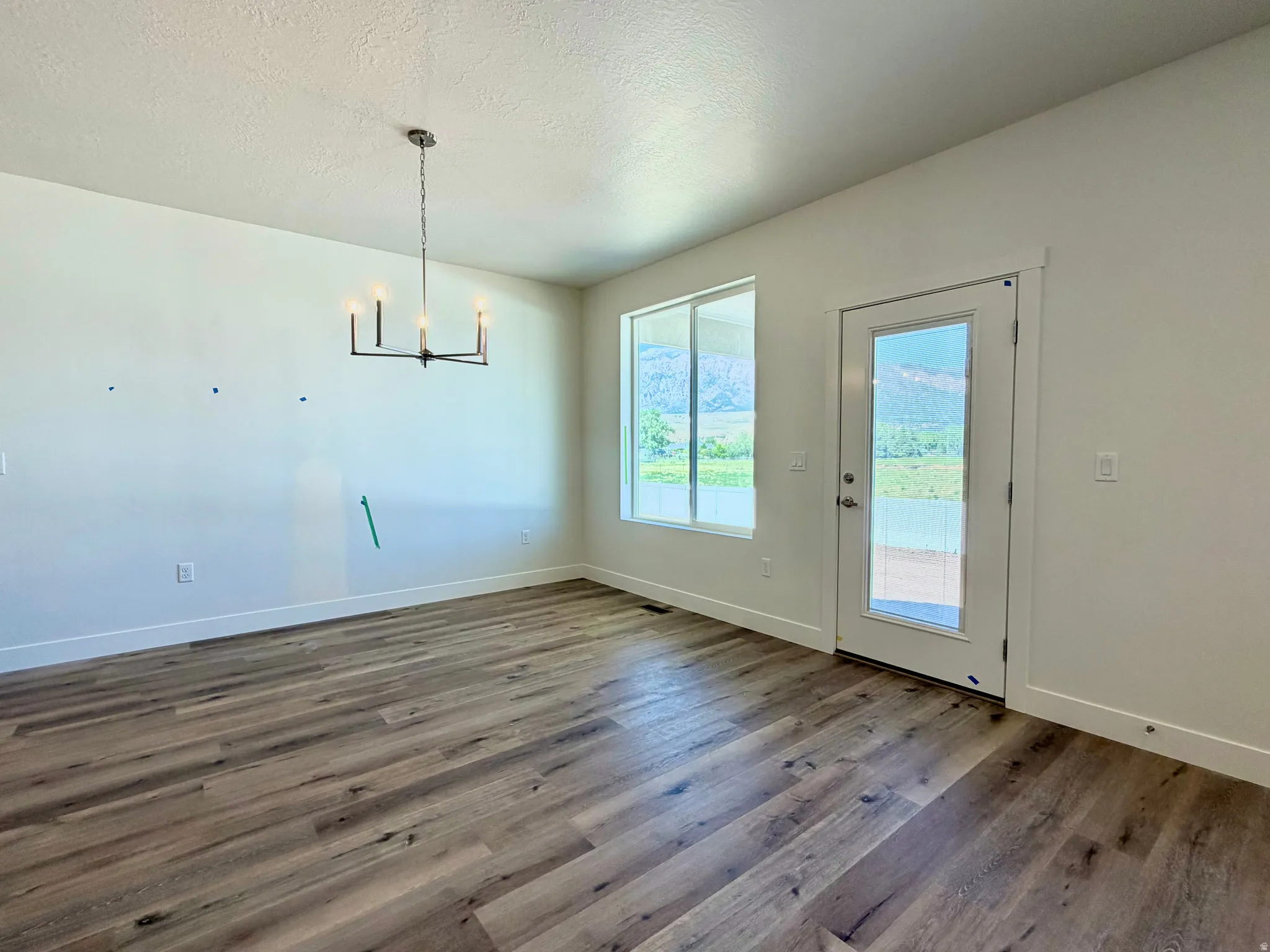Spacious room featuring wood-finish flooring, white walls, and a modern chandelier