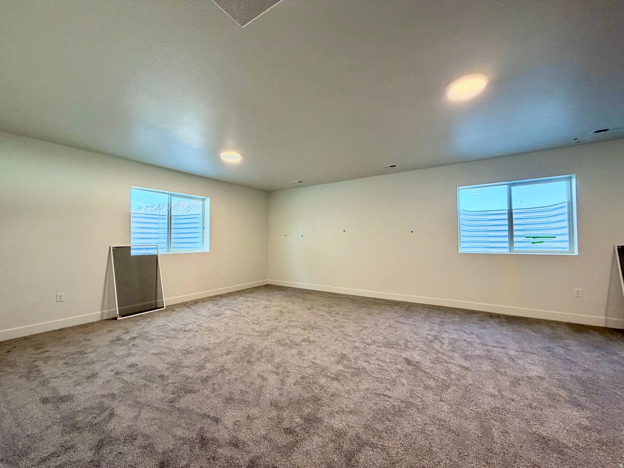Spacious room featuring gray carpet, light-colored walls, and two egress windows