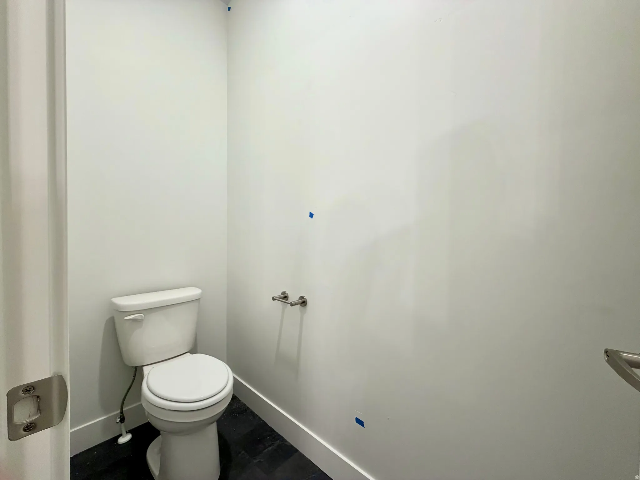 Bathroom featuring a modern white toilet, dark tile flooring, white walls, white trim, and a chrome toilet paper holder