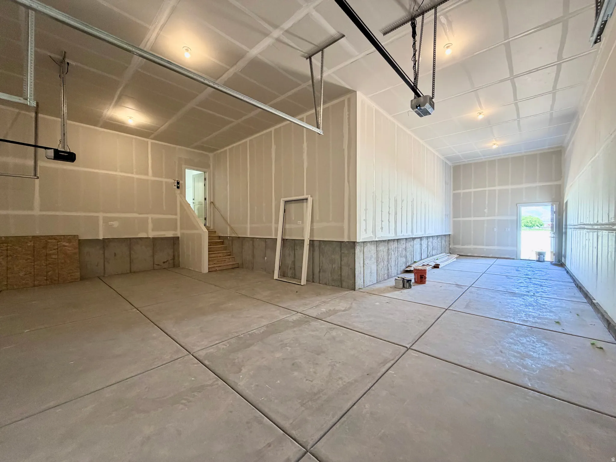 Spacious garage with concrete flooring, drywall-finished walls, built-in staircase, and integrated ceiling lighting